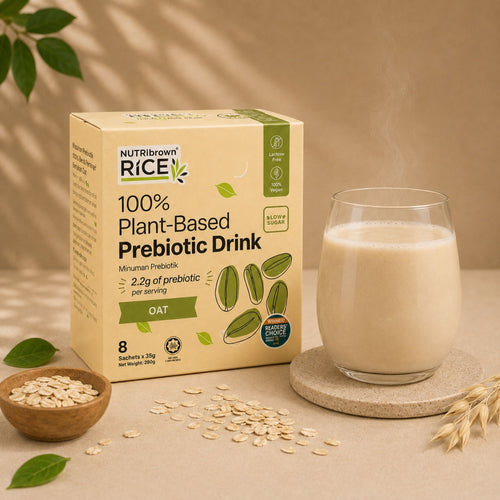 A box of NutriBrown Rice 100% Plant-Based Prebiotic Drink in Oat flavor, shown next to a glass of the creamy beige drink on a coaster, with oats and leaves in a styled setting.